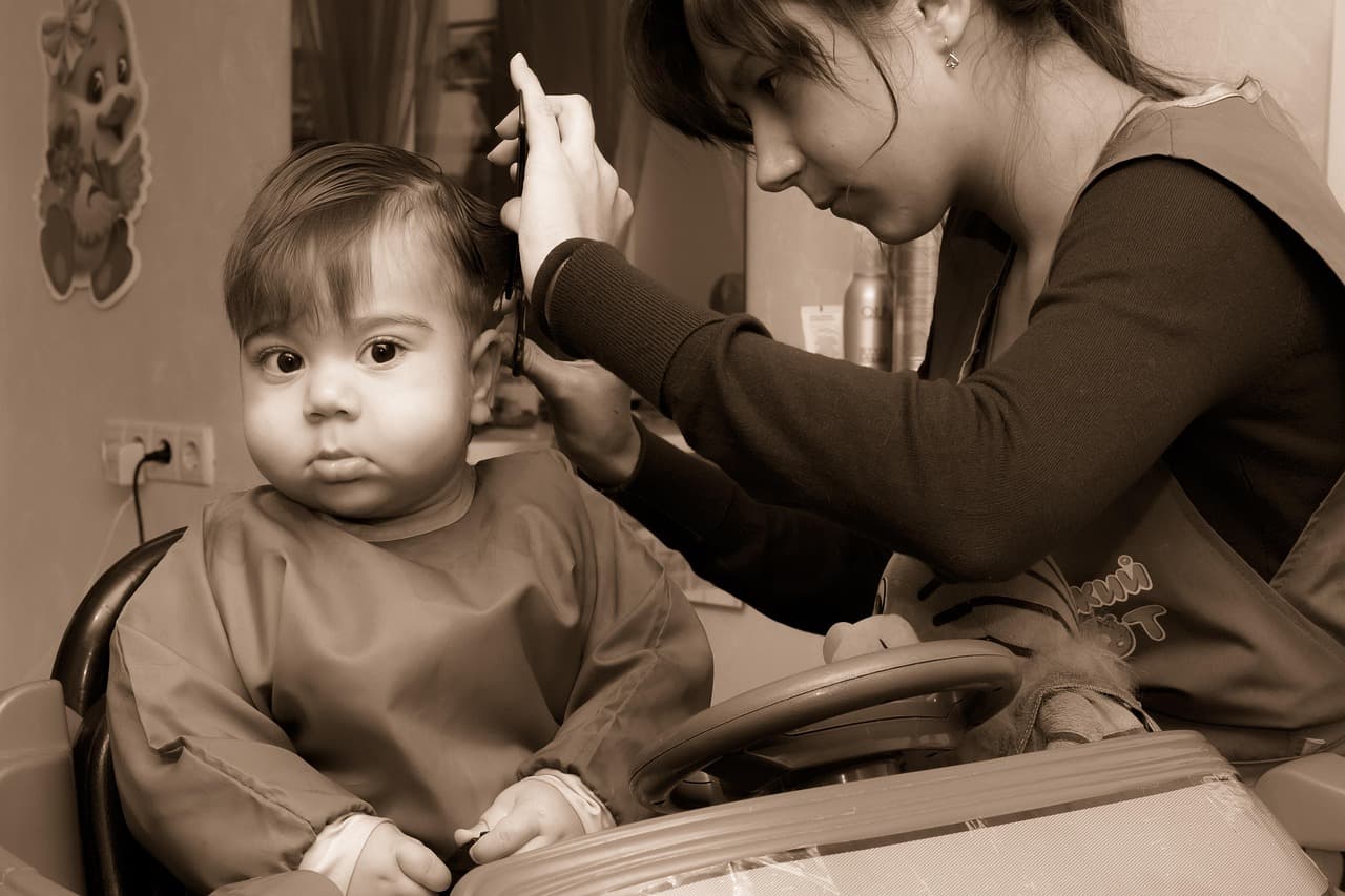 A toddler in a cape sitting very still while his hair is trimmed